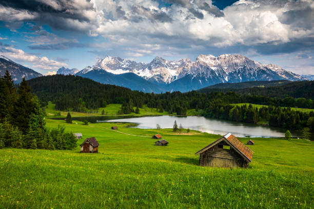 Germany, Bavaria, Karwendel Mountains with Lake Gerold - Tracking shot Idyllic mountain landscape in the Allgäu region of Bavaria in Germany. Beautiful cumulus clouds in the summer sky. Small log cabins surrounded by a green pasture in the foreground. Lake Geroldsee and Karwendel Mountains in the Background. Germany - Europe allgau stock pictures, royalty-free photos & images