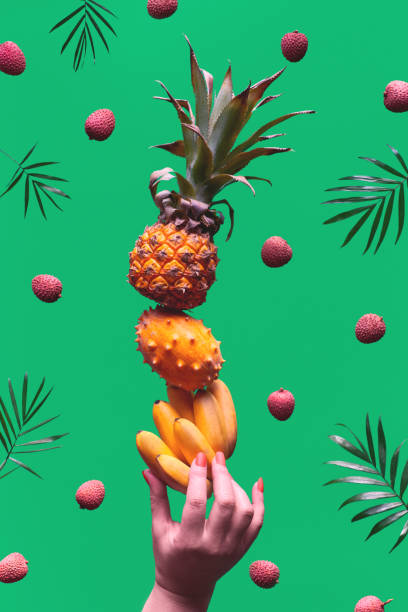 assortiment de fruits tropicaux, pyramide équilibrant o main humaine sur le fond vert. ananas, kiwano, kiwi, litchi et banane - tour faite de fruits exotiques doux et sains. - kawani fruit photos et images de collection