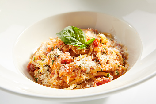 Classical italian spaghetti with tomatoes, tomato sauce, basil, milk mozzarella and parmesan cheese on white restaurant plate isolated. Macro shot of bucatini pasta, pici or stringozzi noodles