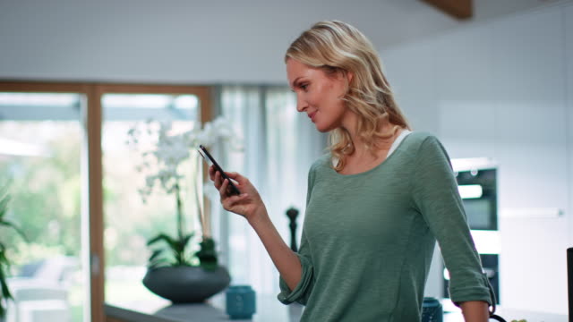 Smiling blond woman using smart phone in kitchen