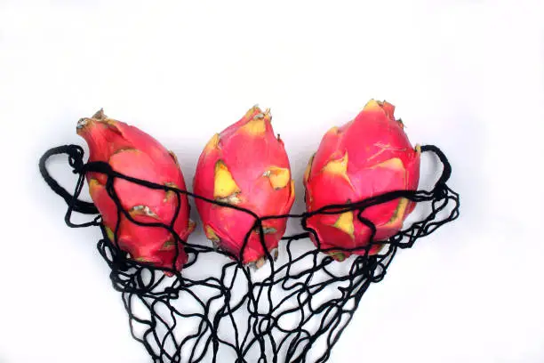 three dragonfruits in a mesh shopping bag isolated on white background. Horizontal image. Flat lay. Image contains copy space