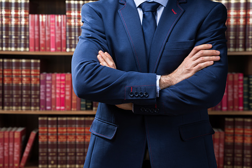 Portrait Of Confident Attorney Standing Arms Crossed Against Bookshelf In Office
