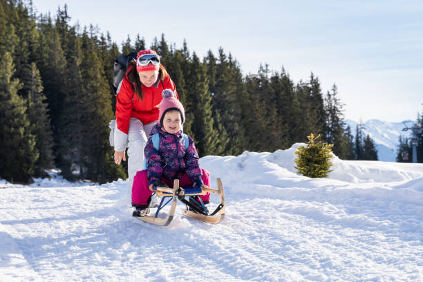 istock Girl Enjoying Sledding With Her Mother Against Winter Forest 1199280430