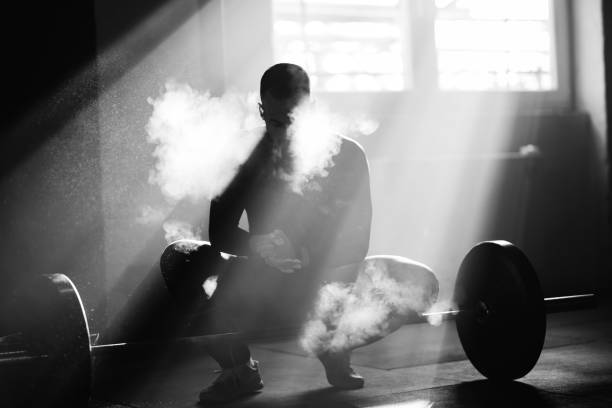 Sportsman applying talcum powder on his hand before weightlifting in a gym. Black and white photo of muscular build man using sports chalk om his hands before exercising with a barbell in a gym. crossfit chalk weightlifting weight training stock pictures, royalty-free photos & images