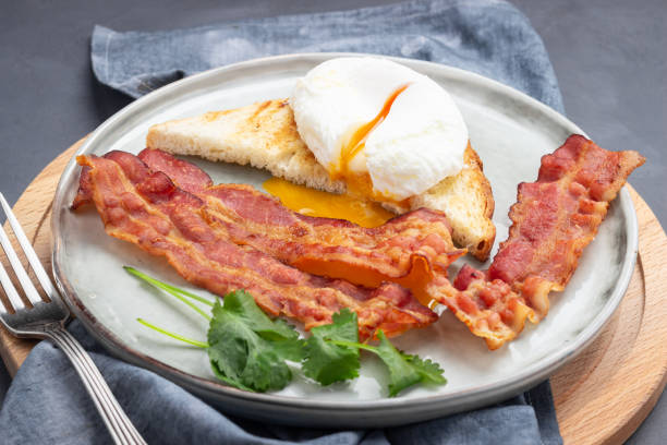 istock Fried bacon pieces and poached eggs on a plate. 1199281804