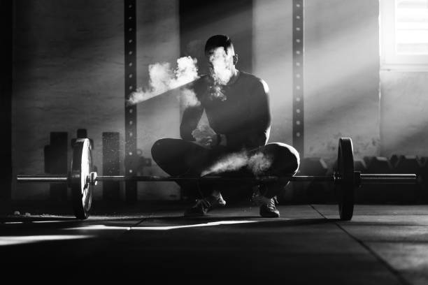Bodybuilder preparing his hands with powder for weightlifting in a gym. Black and white photo of muscular build man using sports chalk while before lifting a barbell on weight training in a gym. crossfit chalk weightlifting weight training stock pictures, royalty-free photos & images