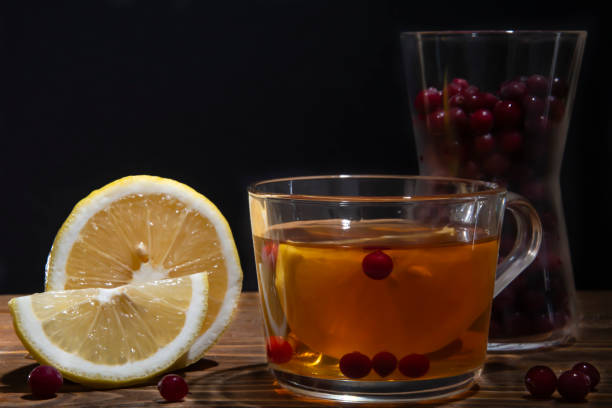 glass cup with tea, lemon and cranberries on a wooden table Glass cup with tea, lemon and cranberries on a wooden table. Black background. кружка stock pictures, royalty-free photos & images