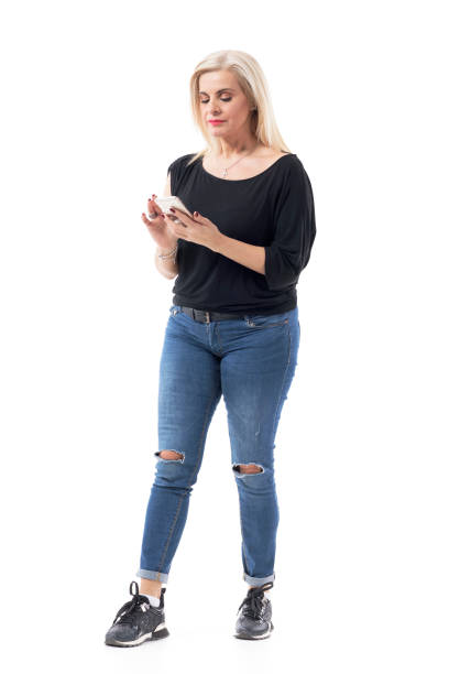 Casual clothed middle age serious woman reading and using smart phone.  Full body length isolated on white background.