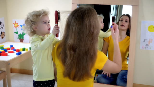 girl combing woman hair in front of mirror