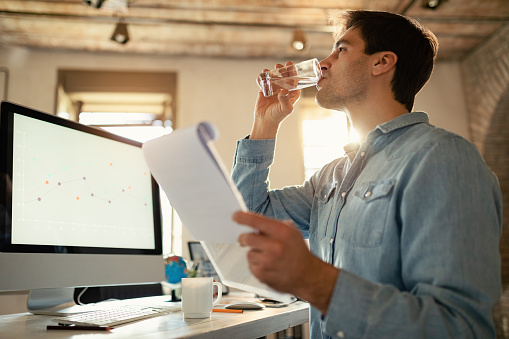 Young freelance worker having a glass of water while working on paperwork in the office.