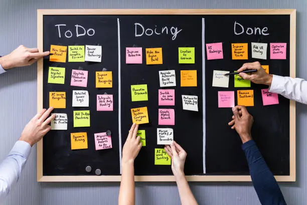 Group Of People Writing On Sticky Notes Attached To Blackboard In Office