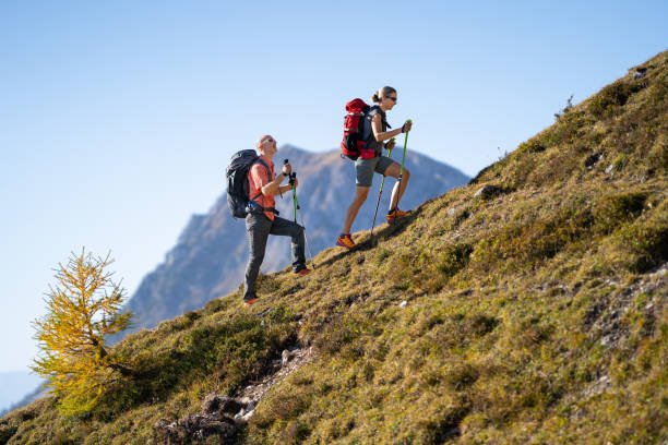 couple on hiking tour in mountains side view hiking couple walking up steep mountain ridge on sunny day in autumn steep stock pictures, royalty-free photos & images