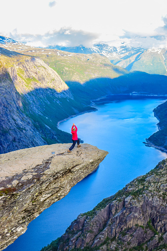 The girl stands in the warrior poses on the Trolltunga, Norway.