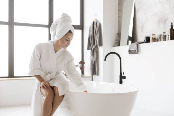 jovencita en el albornoz tocando el agua - bathtub women bathroom relaxation fotografías e imágenes de stock