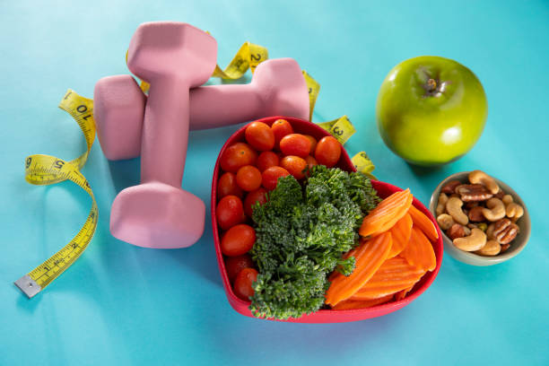 istock Vegetables in a heart bowl with dumbells and an apple on a blue background 1199310168