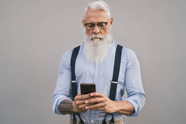 starszy mężczyzna za pomocą smartfona mobilnego i słuchanie muzyki z airpods - moda brodaty mężczyzna pracuje nad marketingiem cyfrowym social media - osoby w podeszłym stylu życia i koncepcji technologii - headphones music mobile phone tattoo zdjęcia i obrazy z banku zdjęć