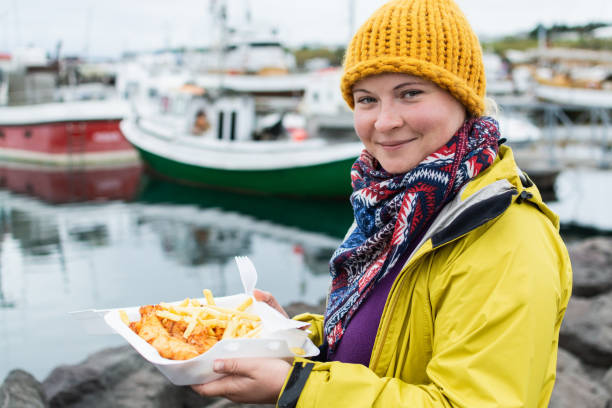 Young woman in yellow raincoat holds a portion of fish and chips in Husavik, Iceland stock photo