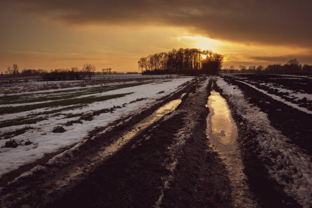 istock Muddy frozen rural road through fields, cloud and sunset, view in winter evening 1199312703