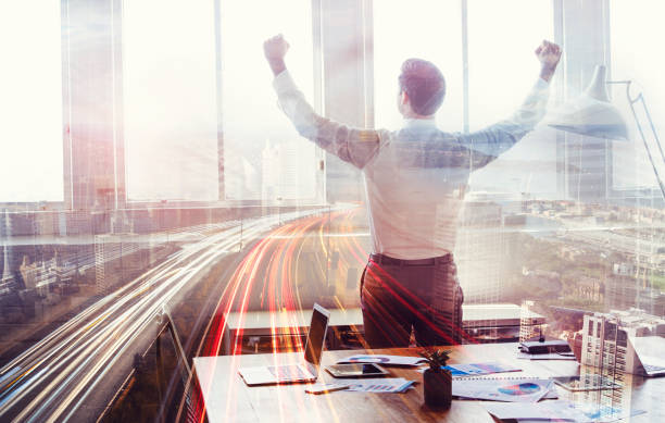 Businessman celebrating with arms outstretched. This is a montage which has a city scape overlaid. Success, vision, architecture; building; development, engineering concept.