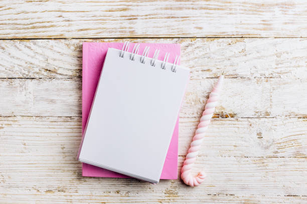 istock Home office desk, plan writing or sketching concept. Open notebook with blank page, cup of coffee and donut covered with pink icing on a white rustic wooden background. Top view. Flat lay 1199320291