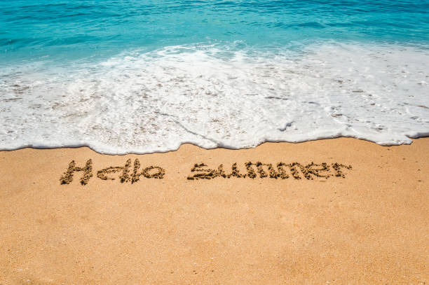 istock Hand written text hello summer on the golden beach sand with coming waves 1199325411