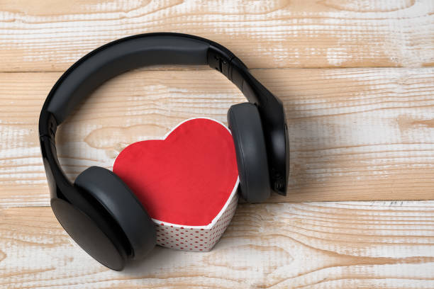 istock Full-size wireless headphones pulled over small red heart-shaped box on a light brown wooden table. Love music concept 1199326894