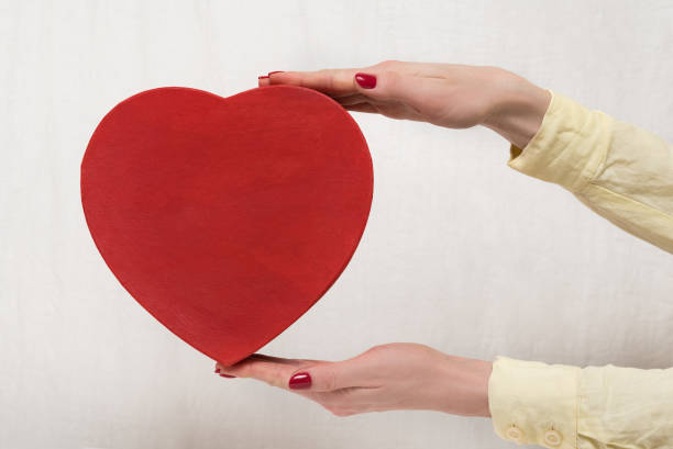 istock Vintage style red heart shaped box on female hands on white background. Front view 1199326914