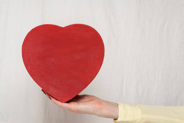 istock Vintage style red heart shaped box on female hand on white background. Front view 1199326919