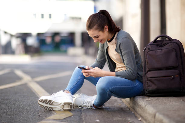 istock happy young woman looking at mobile phone while sitting outside on floor 1199331601
