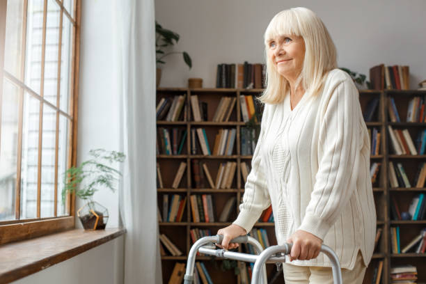 Senior woman with disability recovery at home walking frames looking out the window dreaming stock photo
