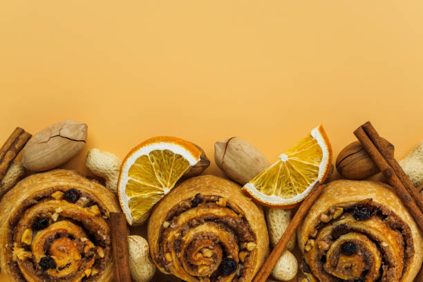 istock Cinnamon rolls, raisins and nuts. Pecans, peanuts and lemon slices on orange background with copy space 1199335338