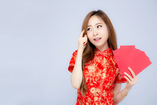 Beautiful portrait young asian woman cheongsam dress smiling and think idea holding red envelope on white background, girl wear qipao celebrate with exciting, happy Chinese New Year, holiday concept.