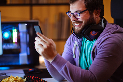 Bearded man typing on phone while sitting in front of his desktop computer