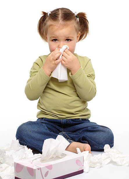 A little girl on the floor blows her nose with a tissue stock photo