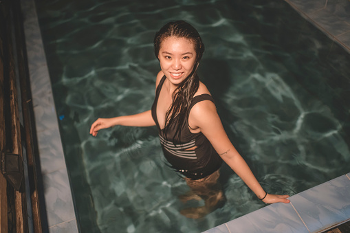 an asian chinese teenage girl swimming at night in her swimming pool in front of her house