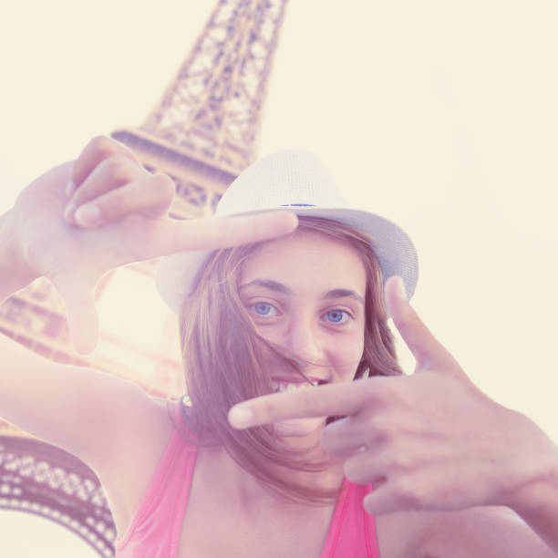 Cheerful woman making photo frame with her fingers at Eiffel tower.She is having a great time. Love Paris.