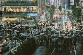 渋谷交差点の雨の夕方に傘をさす歩行者グループ、東京の交通量の多い街の交通と都市の建物を背景に