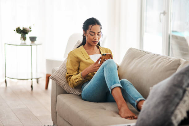 Checking my social media Cropped shot of an attractive young businesswoman sitting on her couch and using her cellphone while at home small business saturday stock pictures, royalty-free photos & images
