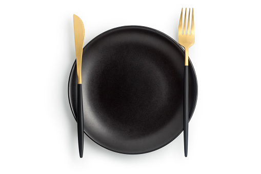 Fork and knife on a empty black plate, Isolated on white background. Top view.