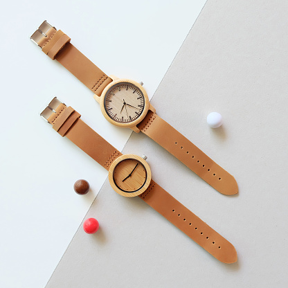 Top view of 2 wooden watches on white and brown color background. Sphere shape decorative objects and leather band watch on soft color background.