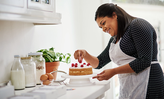 Cropped shot of a woman decorating a cake in her kitchen
