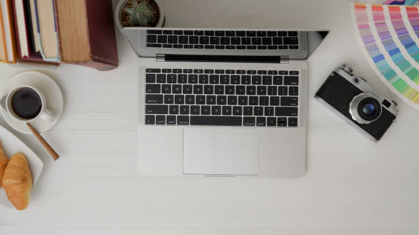 top view of designer workspace with laptop, camera, colour swatch, breakfast and decorations on white desk top view of professional designer workspace with laptop, camera, colour swatch, breakfast and decorations on white desk background food sample cups stock pictures, royalty-free photos & images