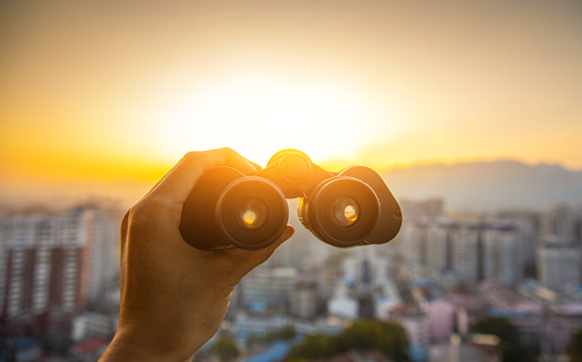Hand holding black binoculars at city sunset