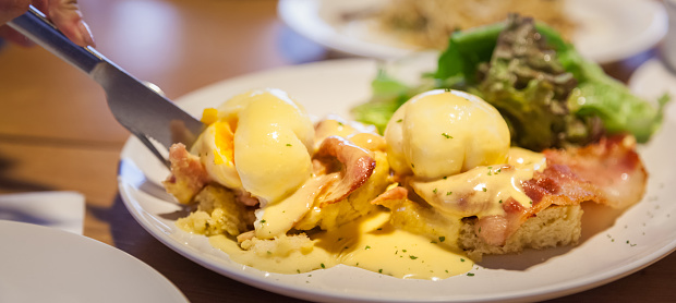 Selective Focused Eggs Benedict, sandwich consists of 2 halves of English muffin topped with poached egg, bacon or ham and hollandaise sauce. American breakfast or brunch dish. Morning meal concept