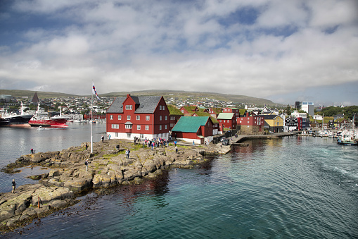 Tórshavn, Faroe Islands - July 19, 2017: Historic red houses of the parliament Tinganes on a sunny summer day, Torshavn, Streymoy, Faroe Islands. Tinganes is the historic location of the Faroese landsstýri (government), and is a central part of Tórshavn. The name Tinganes means 'parliament jetty' or 'parliament point' in Faroese. Many of the wooden houses on Tinganes were built in the 16th and 17th centuries and have the typical red color as well as grass roof, that is very common on the Faroe Islands.