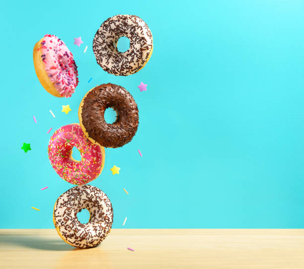 fliegende donuts. mischung aus bunten süßen donuts mit sprinkel auf turqouise blauen hintergrund fällt auf den tisch. - streuen fotos stock-fotos und bilder