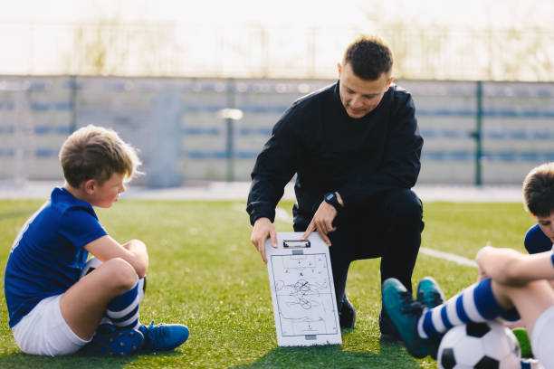 young soccer trainer coach erklärt taktik auf team sports tactics board. kinder während der fußball-coaching-session. jungen im fußballteam hören dem trainer zu - sports uniform blue team event sports activity stock-fotos und bilder