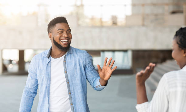 Guy and girl waving hands, greeting each other in the street African american guy and girl waving hands, greeting each other while meeting in the street, panorama with free space waving gesture stock pictures, royalty-free photos & images