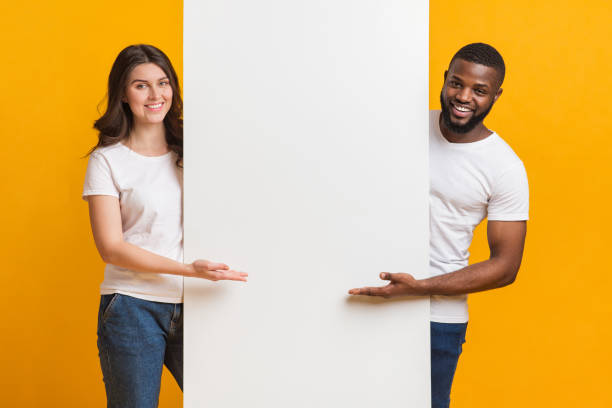 istock Smiling Multiracial Couple Holding And Pointing At White Advertisement Board 1199396122