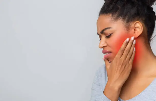 Sad young afro woman having wise teeth pain, touching her inflamed cheek, free space